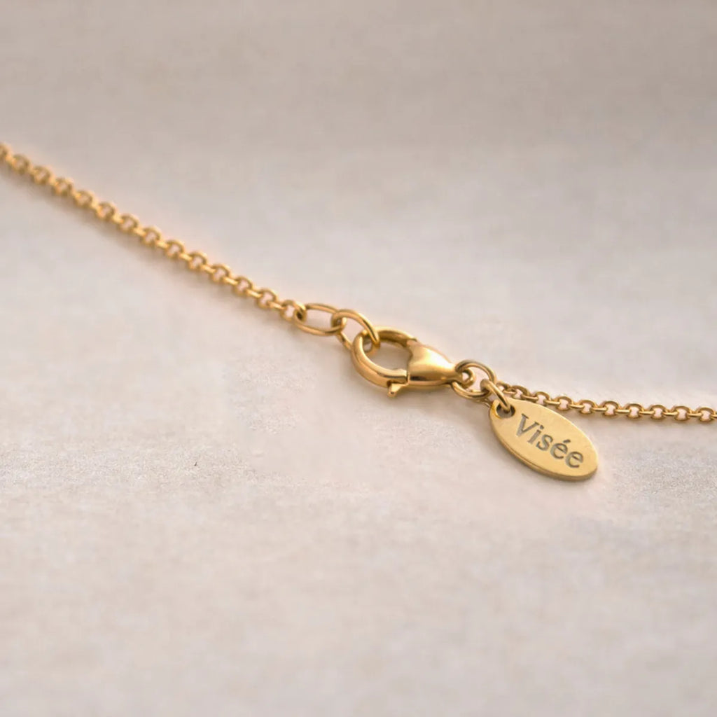 Gros plan sur le fermoir mousqueton du bracelet personnalisé Mon choix avec petite médaille Visée, sur fond beige texturé