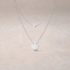 Collier Visée Complice double chaîne perle et médaille acier inoxydable argenté, sur fond beige texturé