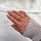 Bague ajustable Coeur battant, en acier doré en forme de cœur finement martelé, ornée d'une étoile brillante au centre, portée à la main sur fond beige. 