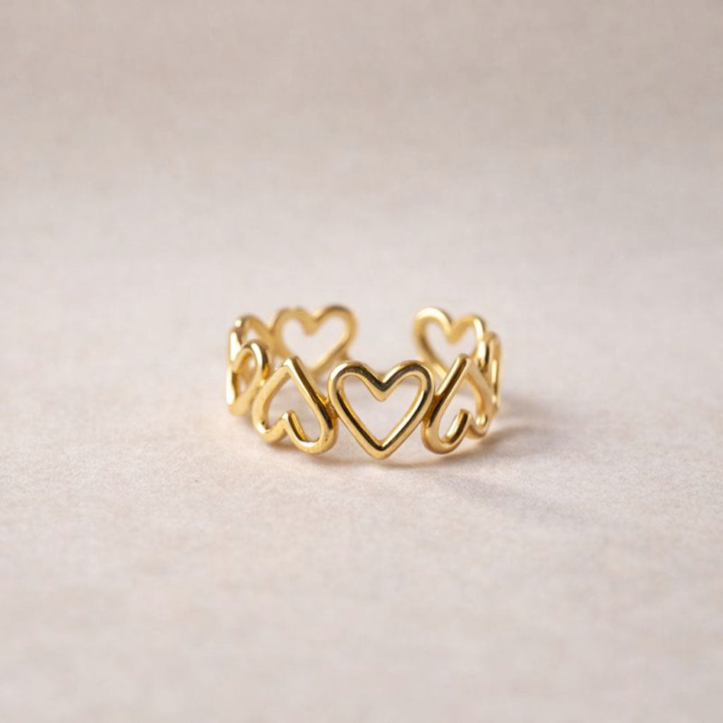 Bague ajustable Mon message, en acier inoxydable doré, orné de cœurs, posée en gros plan sur un support texturé beige clair.