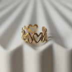 Bague ajustable Mon message, en acier inoxydable doré, orné de coeurs, posée en gros plan sur un support texturé beige clair.