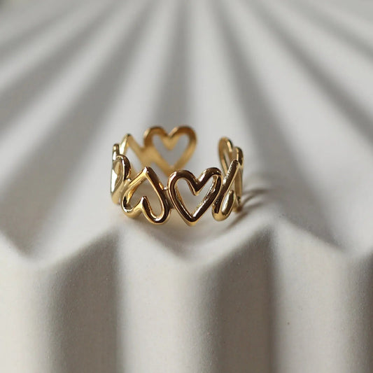 Bague ajustable Mon message, en acier inoxydable doré, orné de coeurs, posée en gros plan sur un support texturé beige clair.