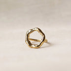 Bague Mon tout, au design cercle martelé en acier inoxydable doré, posée sur un décor beige texturée.