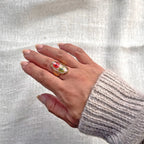 Bague ajustable Mon rythme, en acier inoxydable doré, ornée de deux fleurs séchées rouge et verte, portée à la main.