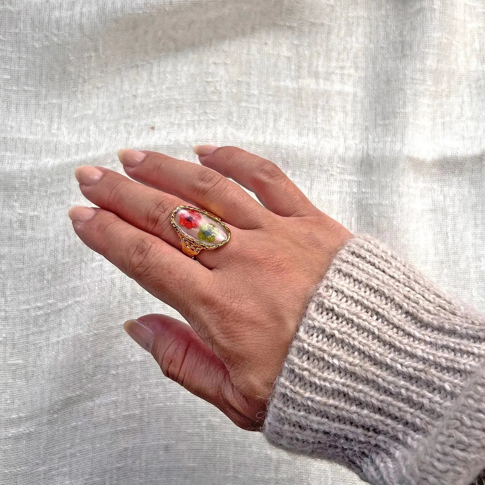 Bague ajustable Mon rythme, en acier inoxydable doré, ornée de deux fleurs séchées rouge et verte, portée à la main.