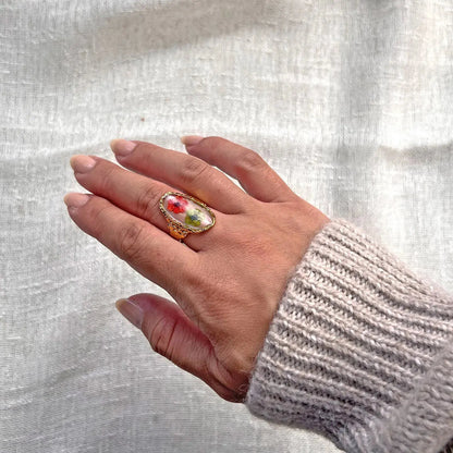 Bague ajustable Mon rythme, en acier inoxydable doré, ornée de deux fleurs séchées rouge et verte, portée à la main.