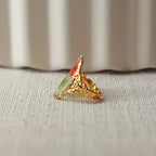 Bague ajustable Mon rythme, en acier inoxydable doré, orné de deux fleurs rouge et verte, posée à plat sur un tissu beige texturé, vue de profil rapprochée.