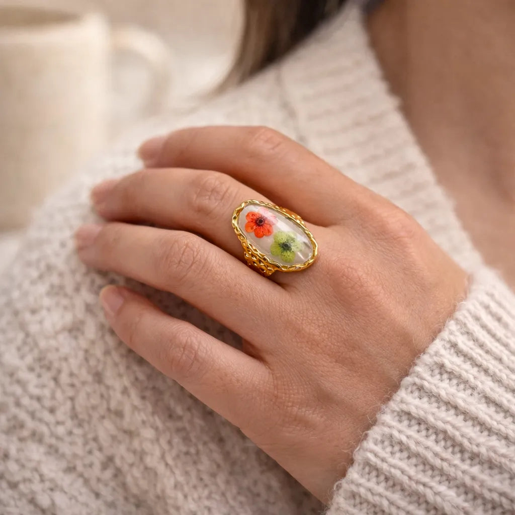 Bague ajustable Pétale, en acier inoxydable doré, ornée de deux fleurs rouge et verte, portée à la main.