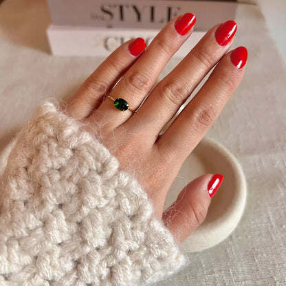 Bague "Mes Facettes" ajustable, ornée d'une pierre blanche, portée sur une main féminine au vernis rouge. En arrière-plan, un livre au style inspiré.