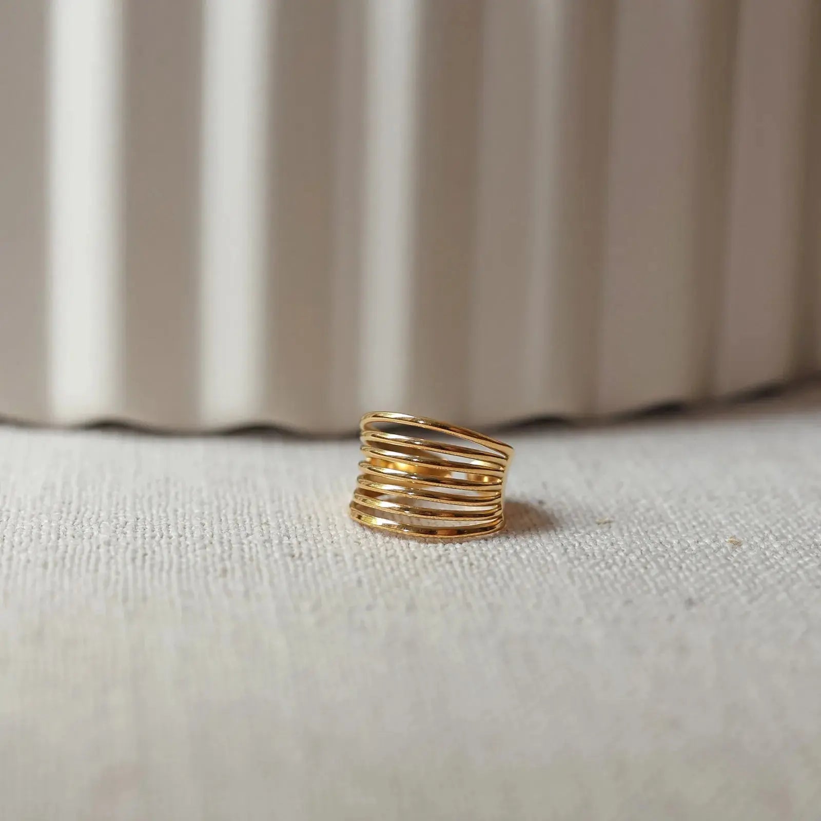 Bague J'ai changé ajustable à plusieurs anneaux en acier inoxydable doré, posée à plat sur un tissu beige plissé avec un bloc flou en arrière-plan.