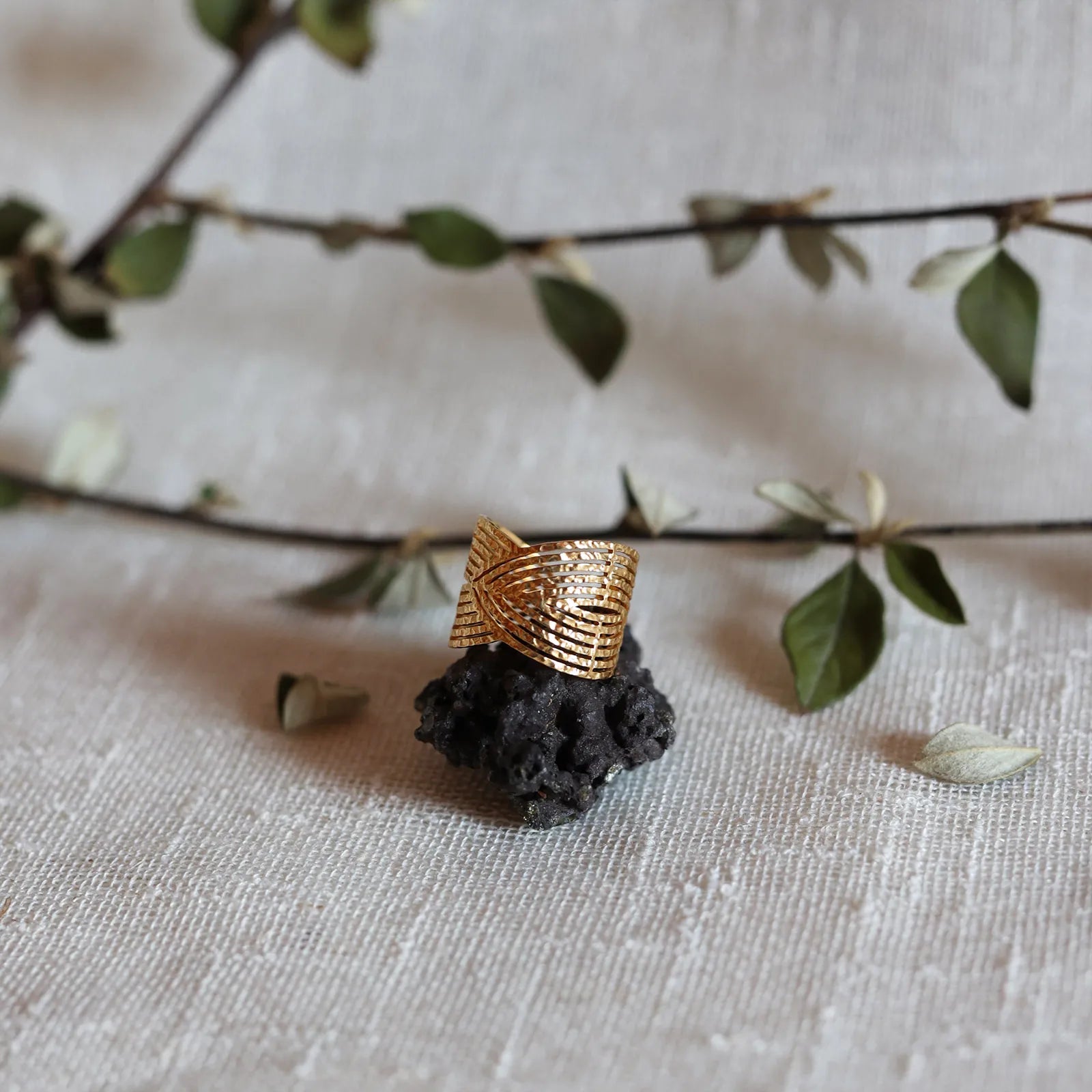Bague Avenir ajustable, au design géométrique en acier inoxydable doré, posée sur une pierre volcanique, sur fond de toile beige et feuillage.