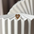 Bague ajustable Coeur battant, en acier doré en forme de cœur finement martelé, ornée d'une étoile brillante au centre, photographiée de face sur un fond beige texturé.