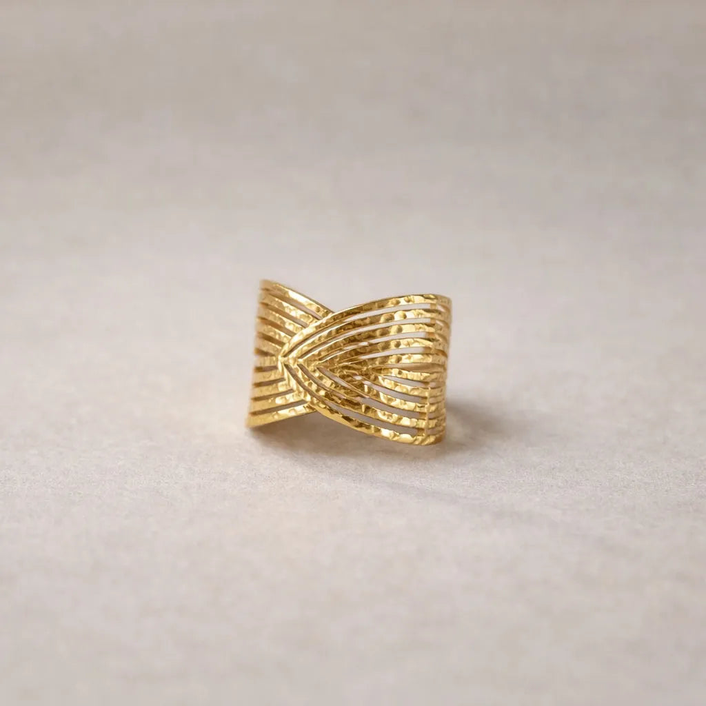Bague Entrelacs ajustable, au design géométrique en acier inoxydable doré, posée sur un fond beige texturés