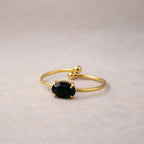 Bagues "Mes Facettes" ajustables, en acier doré, ornées d'une pierre de couleur noire, posées à plat sur un fond beige texturé.