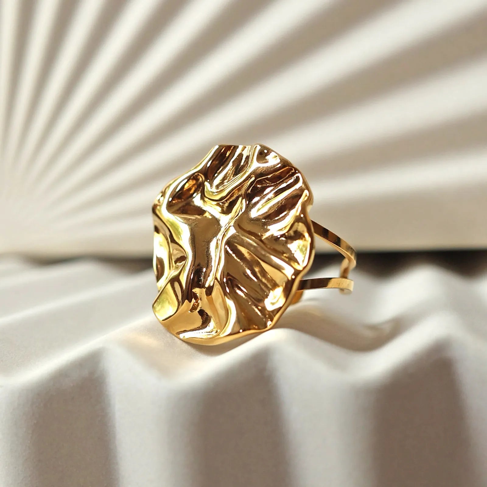 Bague ajustable en acier doré, à motif sculpté, capturée en gros plan sur un fond beige texturé aux reflets doux.