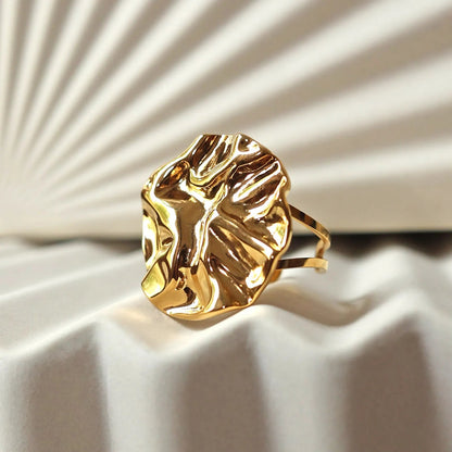Bague ajustable en acier doré, à motif sculpté, capturée en gros plan sur un fond beige texturé aux reflets doux.