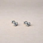 Les boucles d'oreilles Doux de Visée, en forme de cœur en acier argenté, posées sur un fond beige texturé avec une vue de face