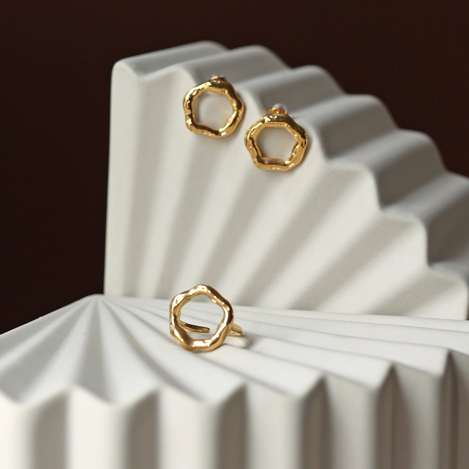 Vue d'ensemble des boucles d'oreilles dorées martelées Source en acier inoxydable et de la bague Mon tout, posées sur un  support texturé beige.