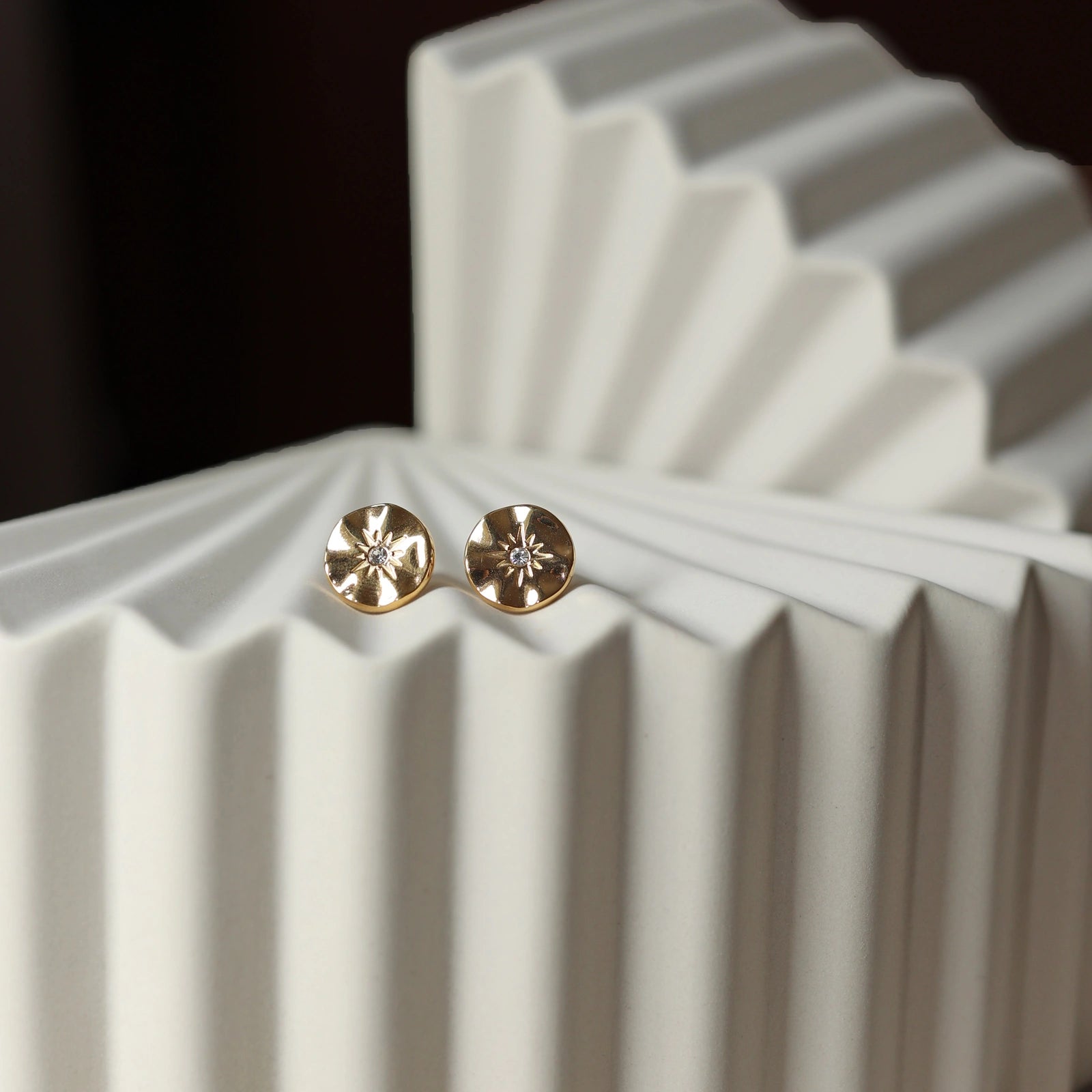 Boucles d’oreilles Céleste dorées motif étoile, serties d'un zircon, posées sur un fond beige - Visée Bijoux.