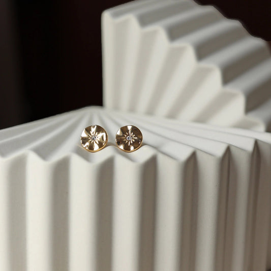 Boucles d’oreilles Céleste dorées motif étoile, serties d'un zircon, posées sur un fond beige - Visée Bijoux.