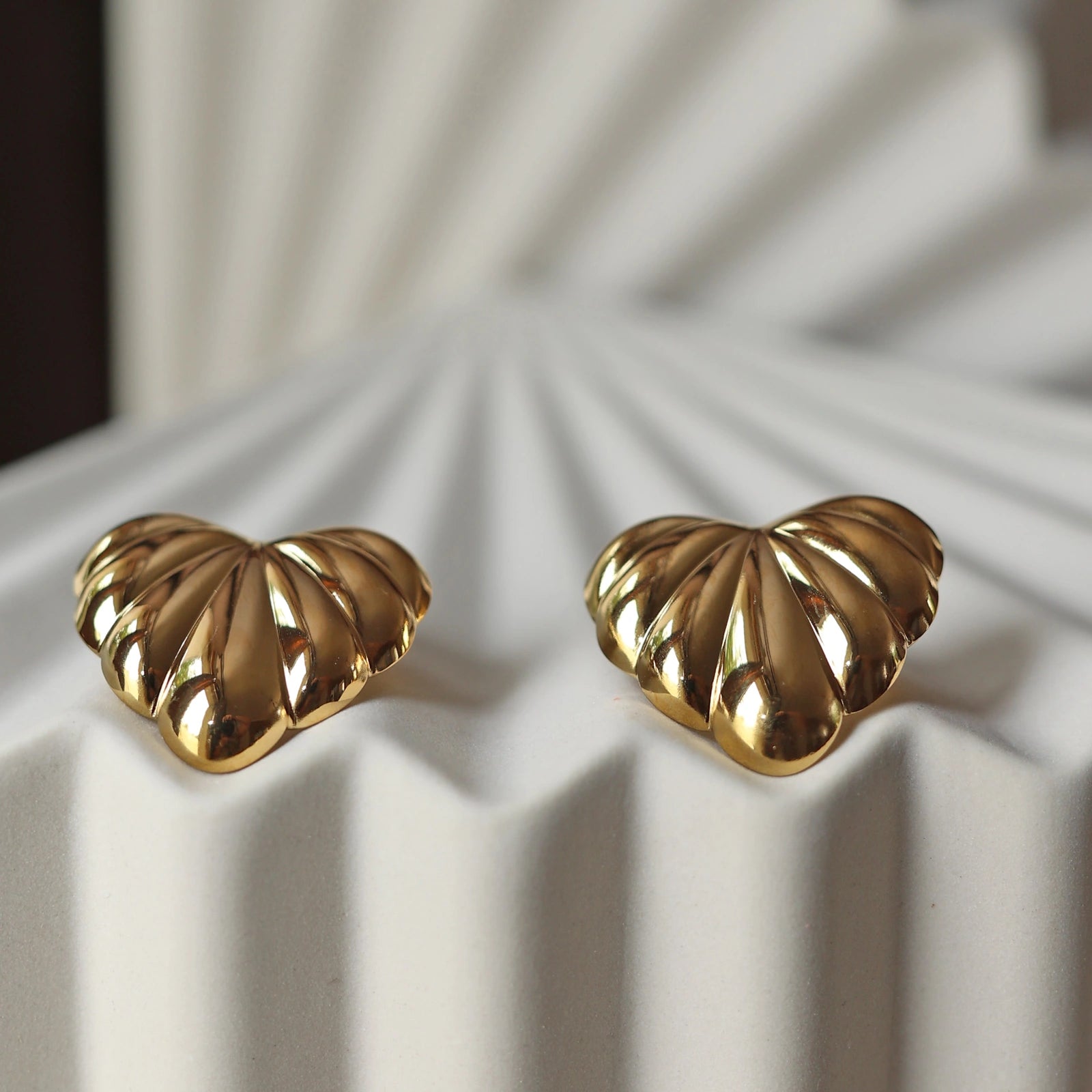 Boucles d'oreilles "Coeur audacieux", en acier inoxydable doré, au design sculpté en forme de coeur, capturées en gros plan sur fond texturé beige.