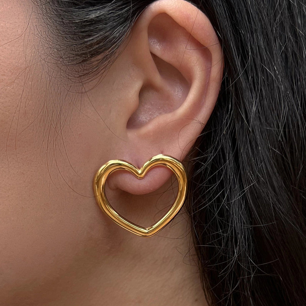 Boucles d'oreilles Douce force en acier doré, grand motif cœur, portées à l'oreille.