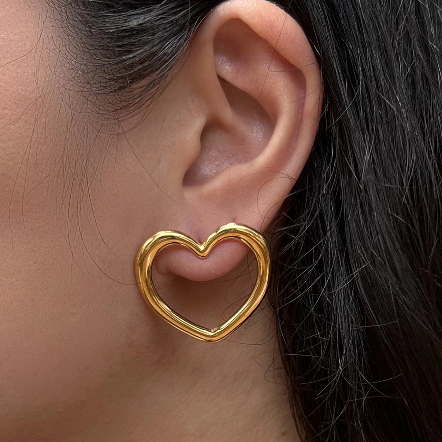 Boucles d'oreilles Douce force en acier doré, grand motif cœur, portées à l'oreille.