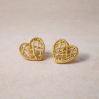 Boucles d'oreilles Etreinte en acier doré, cœurs tressés photographiées en gros plan sur un tissu beige texturé.