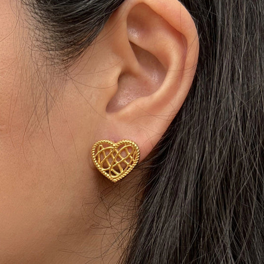 Boucles d'oreilles Etreinte en acier doré, cœurs tressés, portées à l'oreille.