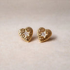 Boucles d'oreilles Promesse, en forme de cœur ornées d'une étoile, en acier inoxydable doré, posées sur un fond beige texturé.