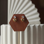 Boucles d'oreilles Intuition en acier doré, coeur délicat serti de pierre scintillante, présentées sur un socle.