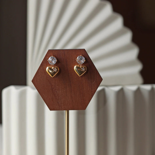 Boucles d'oreilles Intuition en acier doré, coeur délicat serti de pierre scintillante, présentées sur un socle.