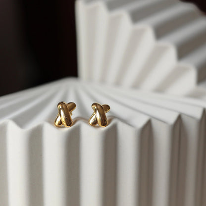 Boucles d'oreilles "Révèle toi", au design croix en acier inoxydable doré, photographiées sur un fond beige texturé.