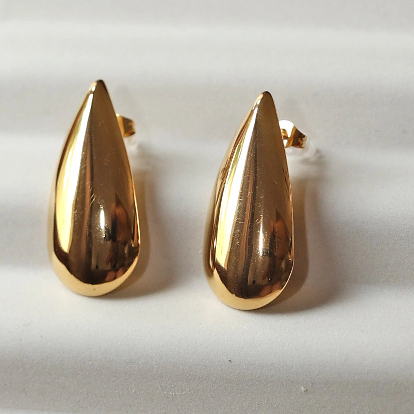 Boucles d'oreilles Larmes assumées en  acier doré, gouttes lumineuses capturées en gros plan.