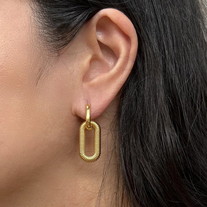 Boucles d'oreilles "J'existe" en acier doré, au design modulable, portées à l'oreille.