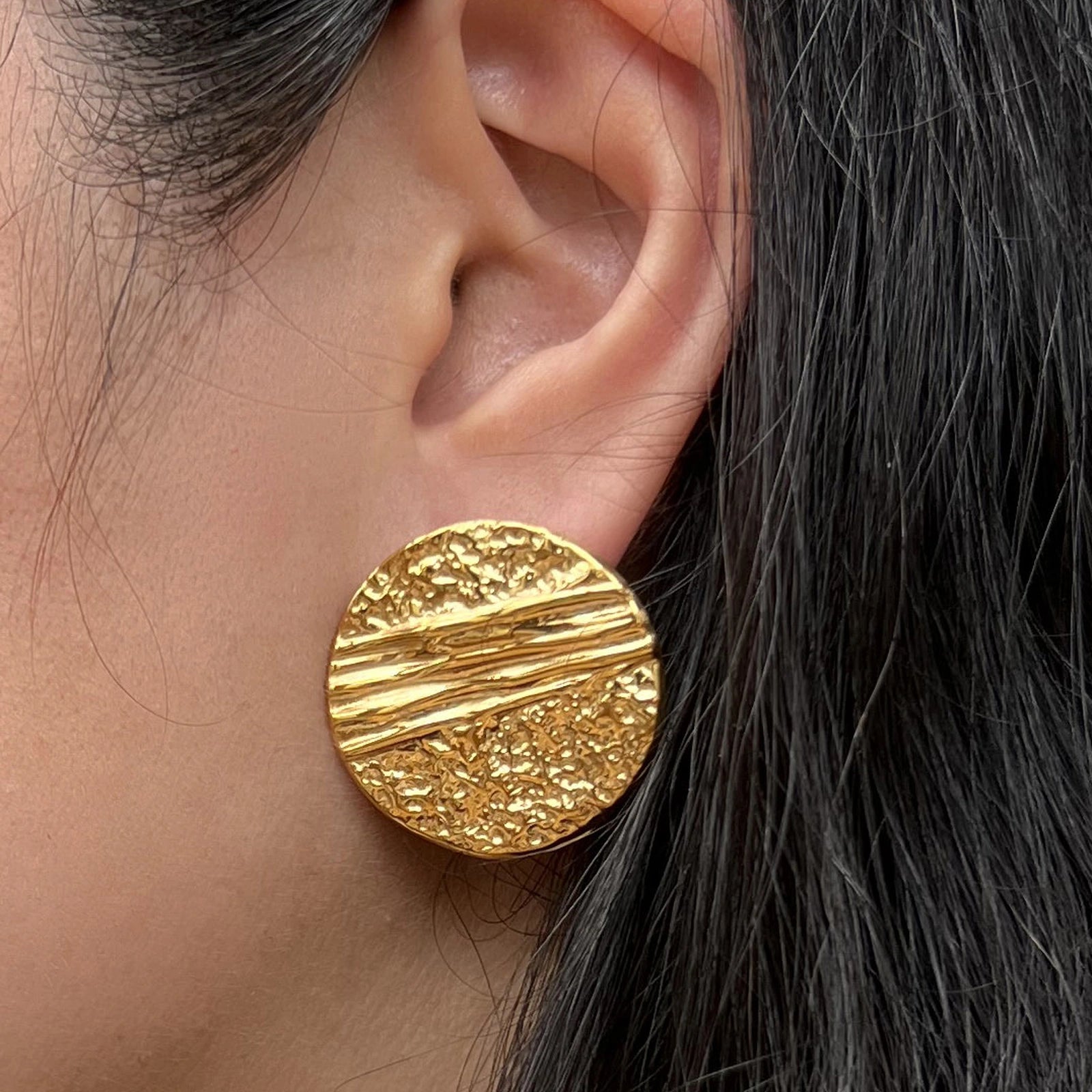Boucles d'oreilles Rayonnante, en acier inoxydable doré, au design rond texturé et éclatant. Portées à l'oreille.