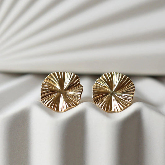 Boucles d'oreilles "Ma raison" en acier doré, au motif floral, photographiées sur un fond plissé beige texturé.