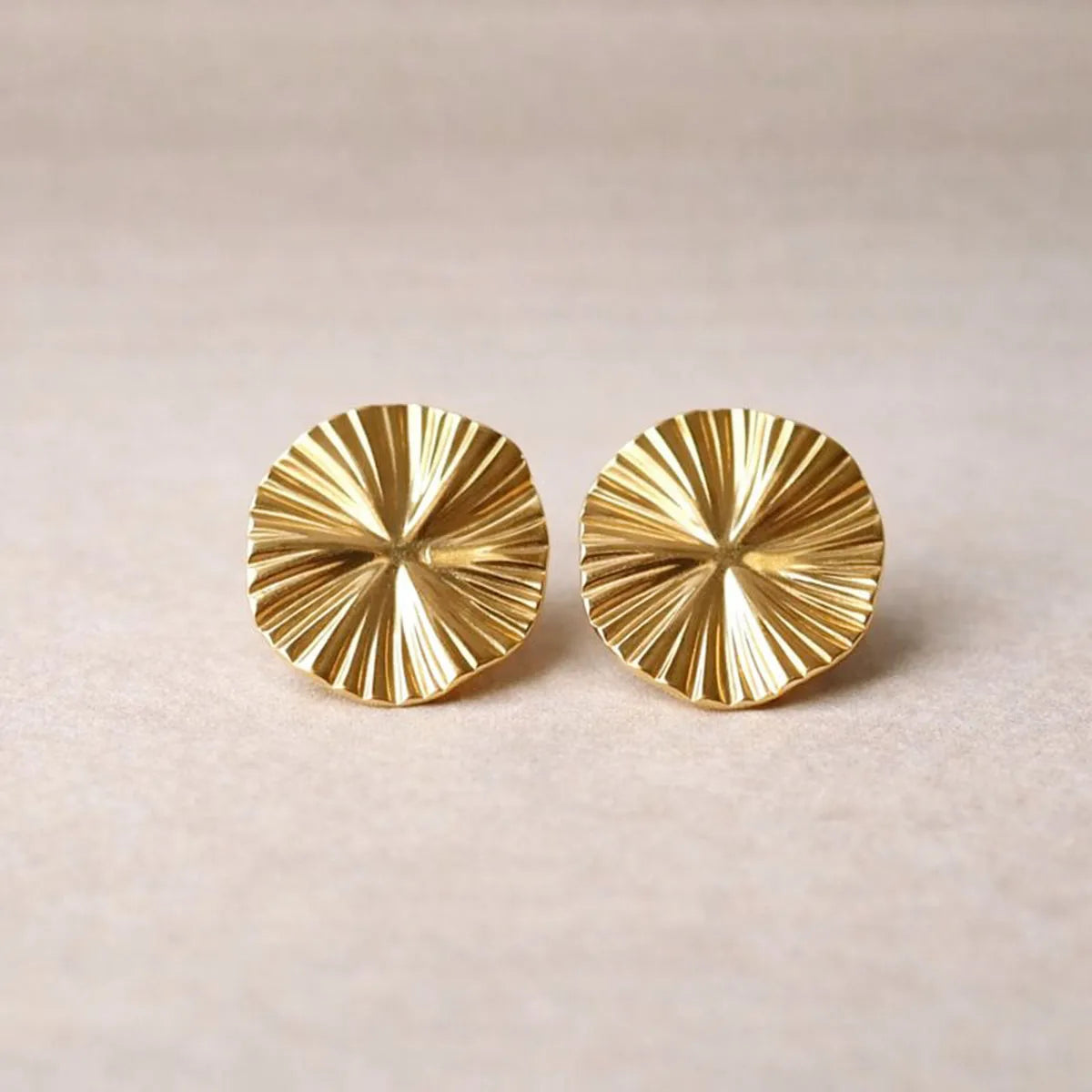 Boucles d'oreilles "Ma raison" en acier doré, au motif floral, photographiées sur un fond  beige texturé.