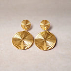 Vue d'ensemble des boucles d'oreilles Vivante pendantes au design solaire strié en acier inoxydable doré, posées à plat sur un fond en toile beige texturé.