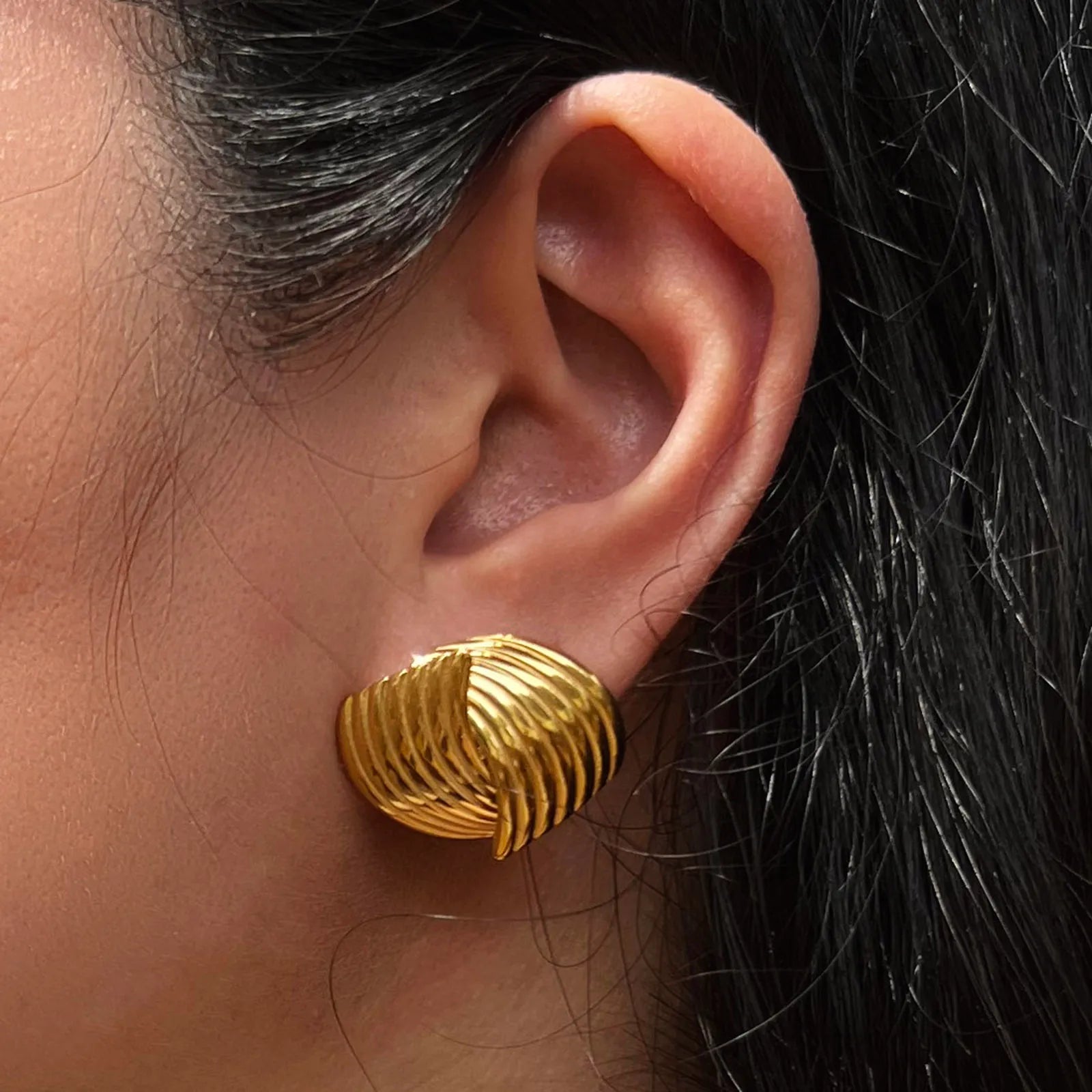 Boucles d’oreilles torsadées Métamorphose en acier inoxydable doré, portées sur une oreille, vue de profil sur mannequin.