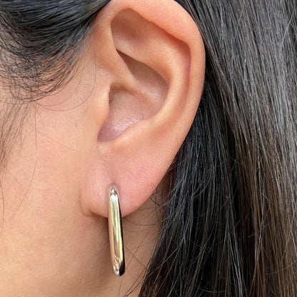 Boucles d'oreilles J'agis, créoles rectangulaires en acier inoxydable argenté, portées sur l'oreille.
