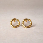 Zoom sur les boucles d'oreilles martelées Naturelle en acier inoxydable doré, posées sur un fond texturé beige.