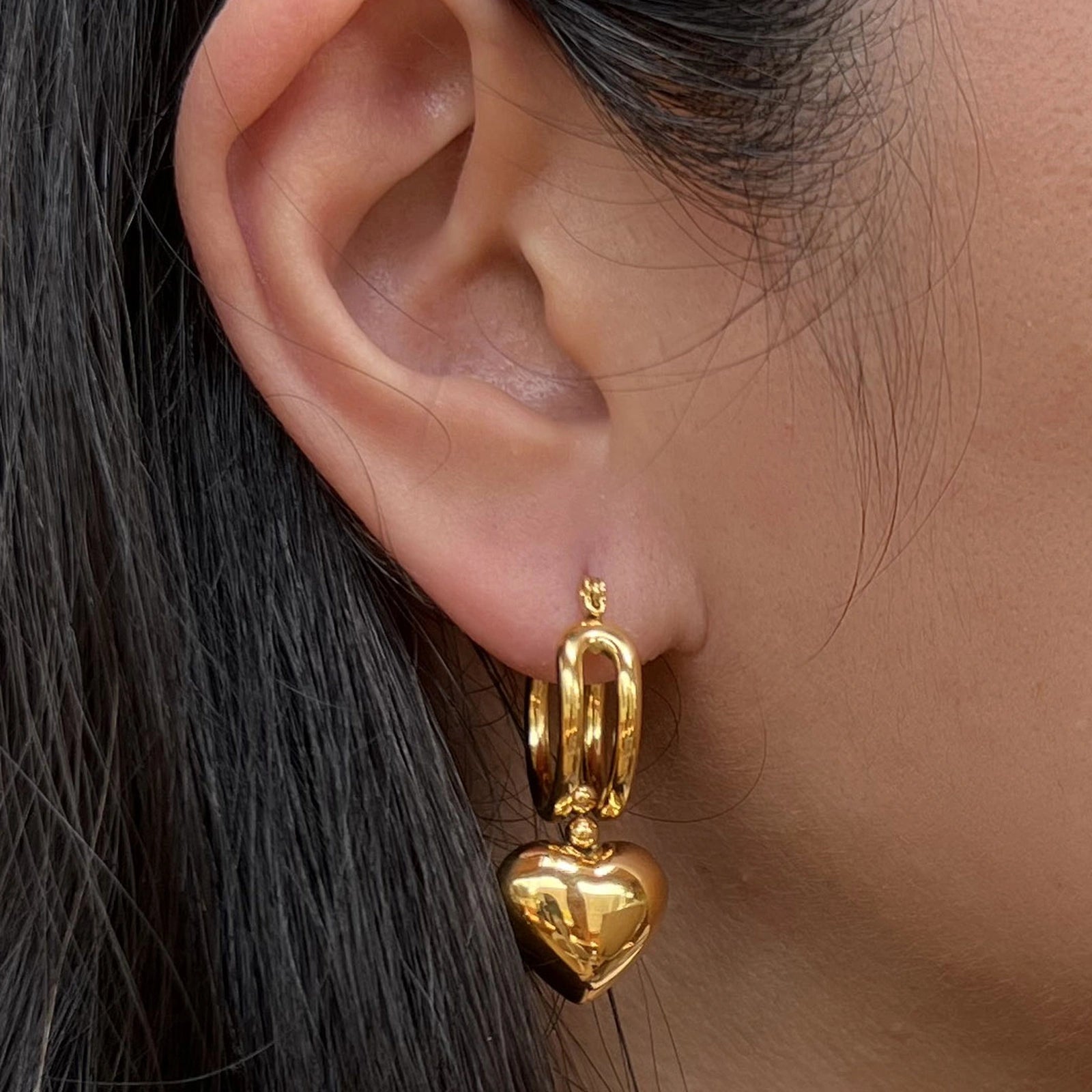 Boucles d'oreilles "Amour suspendu" , avec pendentifs coeurs en acier doré, portées à l'oreille.