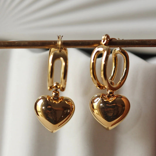 Zoom sur les boucles d'oreilles "Amour suspendu" de Visée, avec pendentifs coeurs en acier doré.