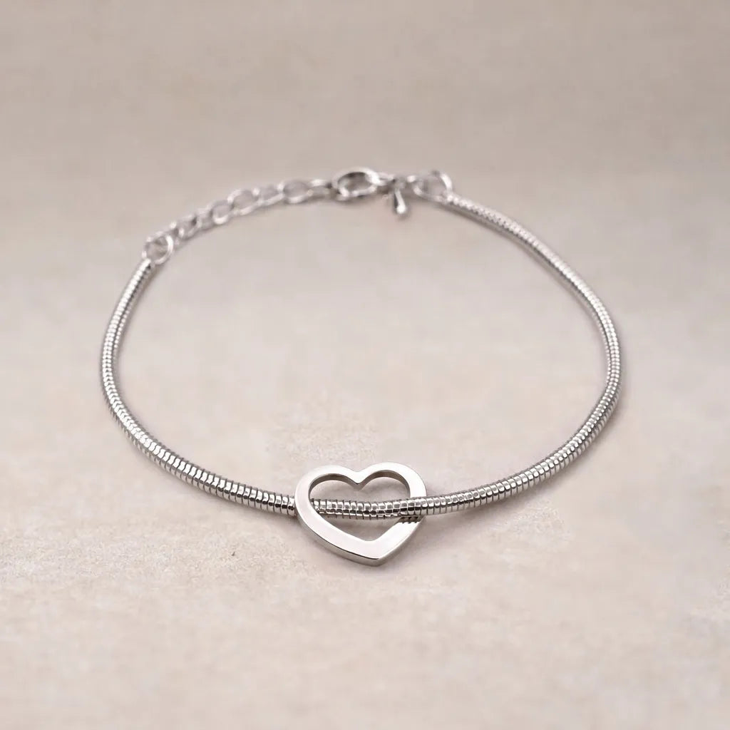 Zoom sur le bracelet "Coeurs" en acier argenté, orné d'un cœur mobile, posé sur un fond beige texturé.