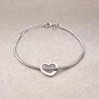 Zoom sur le bracelet "Coeurs" en acier argenté, orné d'un cœur mobile, posé sur un fond beige texturé.