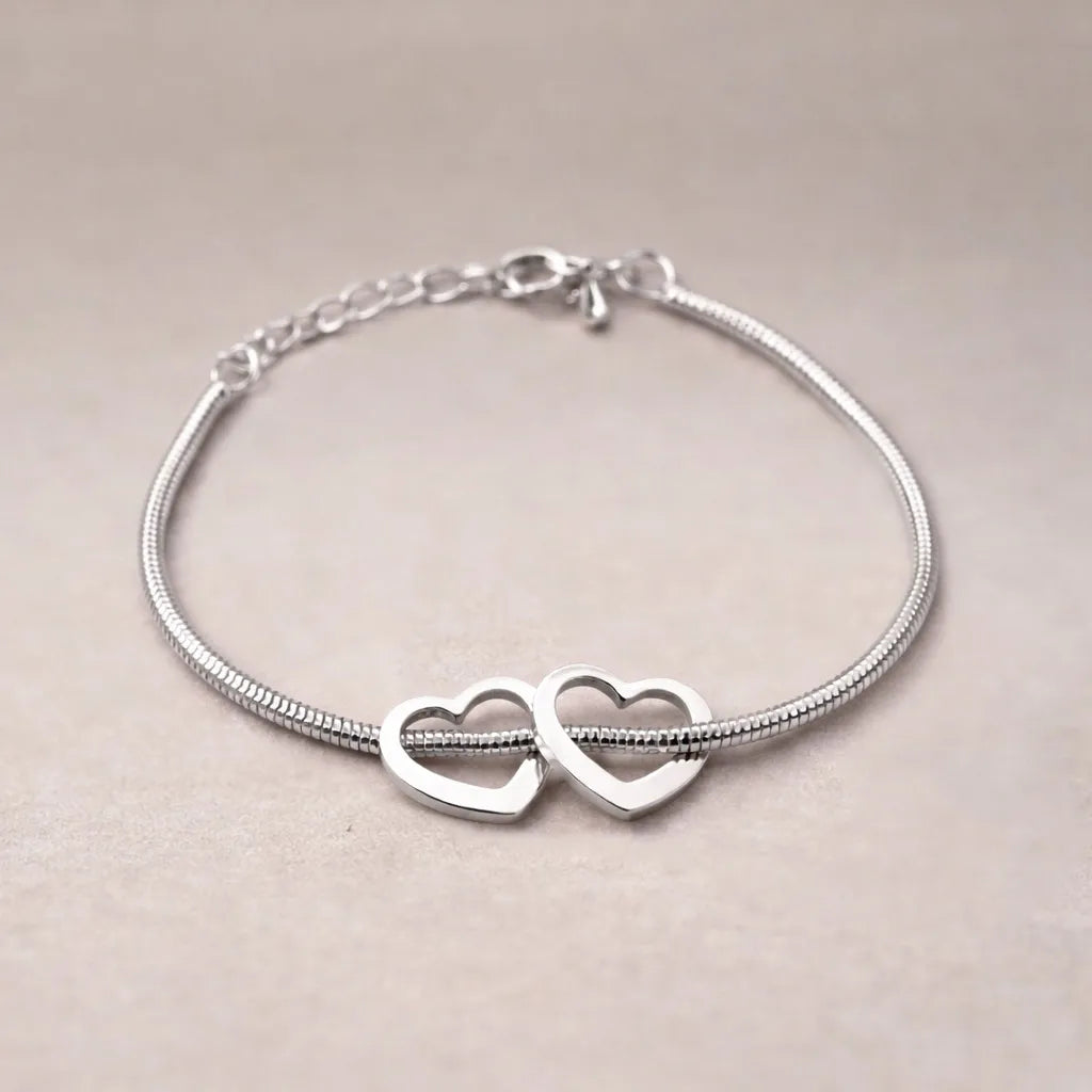 Zoom sur le bracelet "Coeurs" en acier argenté, orné de deux cœurs mobiles, posé sur un fond beige texturé.