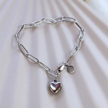 Bracelet Valeur acier inoxydable argenté, avec breloque cœur personnalisable, posé sur un fond beige texturé.