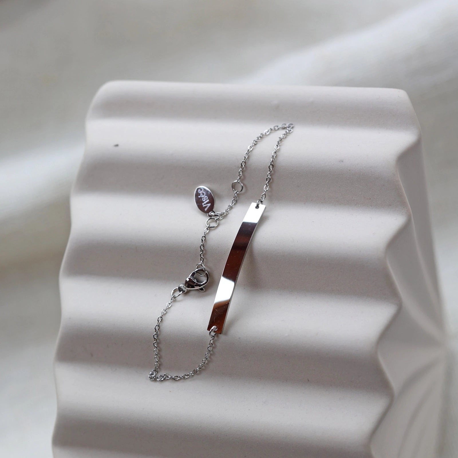 Bracelet gourmette "Sincérité" en acier inoxydable argenté,  personnalisable, posé sur un fond beige texturé.