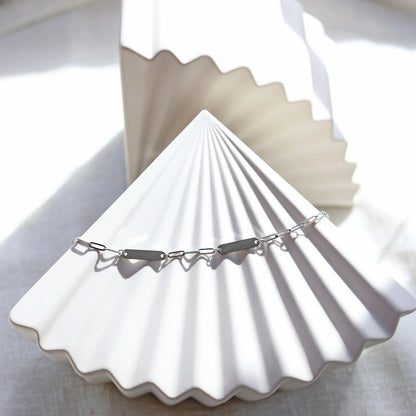 Bracelet "Expression" en acier inoxydable argenté, à personnaliser avec deux plaques gravables, présenté sur un fond beige texturé.